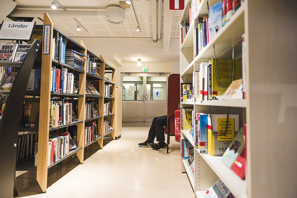 Bild från biblioteket, med bokhyllor och en läsfåtöljer som det sticker ut ett par ben ifrån