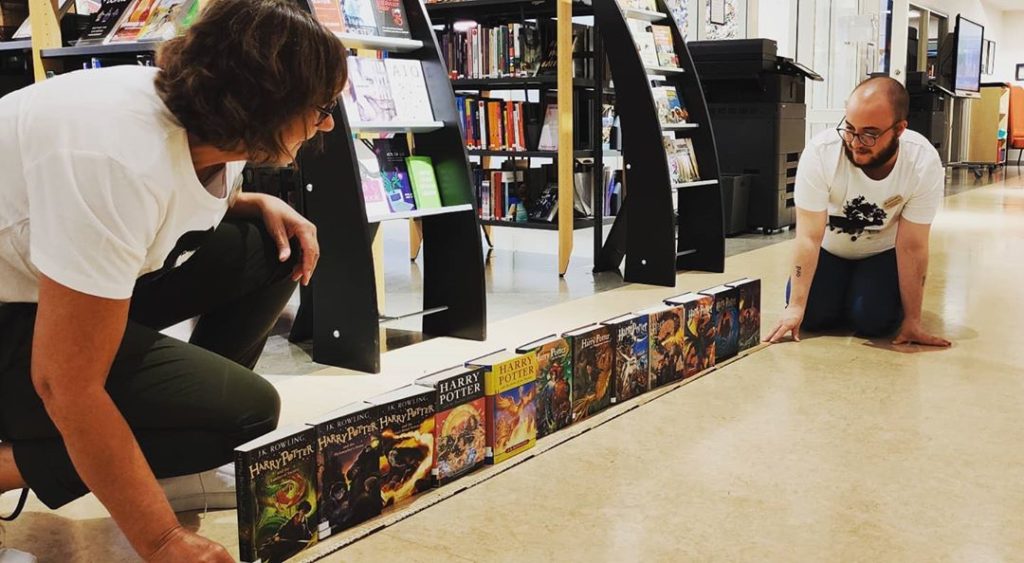 Elisabet och Sebastian som sitter på huk på golvet i biblioteket och mäter längden av bibblans Harry Potter-böcker med en tumstock
